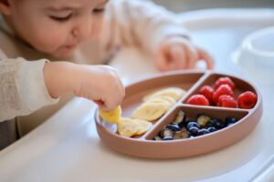Baby picking up banana slice from plate 